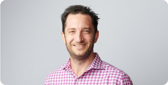 Portrait of Josh Lefkowitz smiling in a checkered red button up shirt.