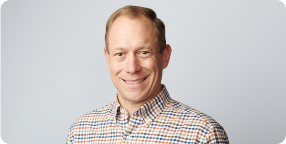 Portrait of Patrick Gardner smiling in a checkered button up shirt.