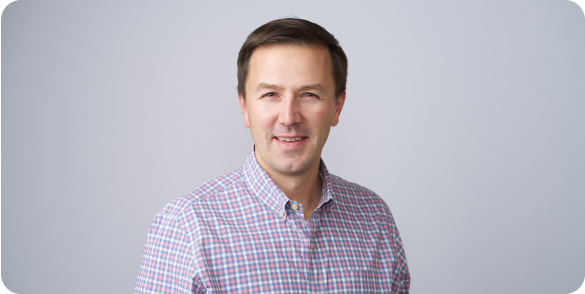 Portrait of Tom Hofmann smiling in a checkered button up shirt.